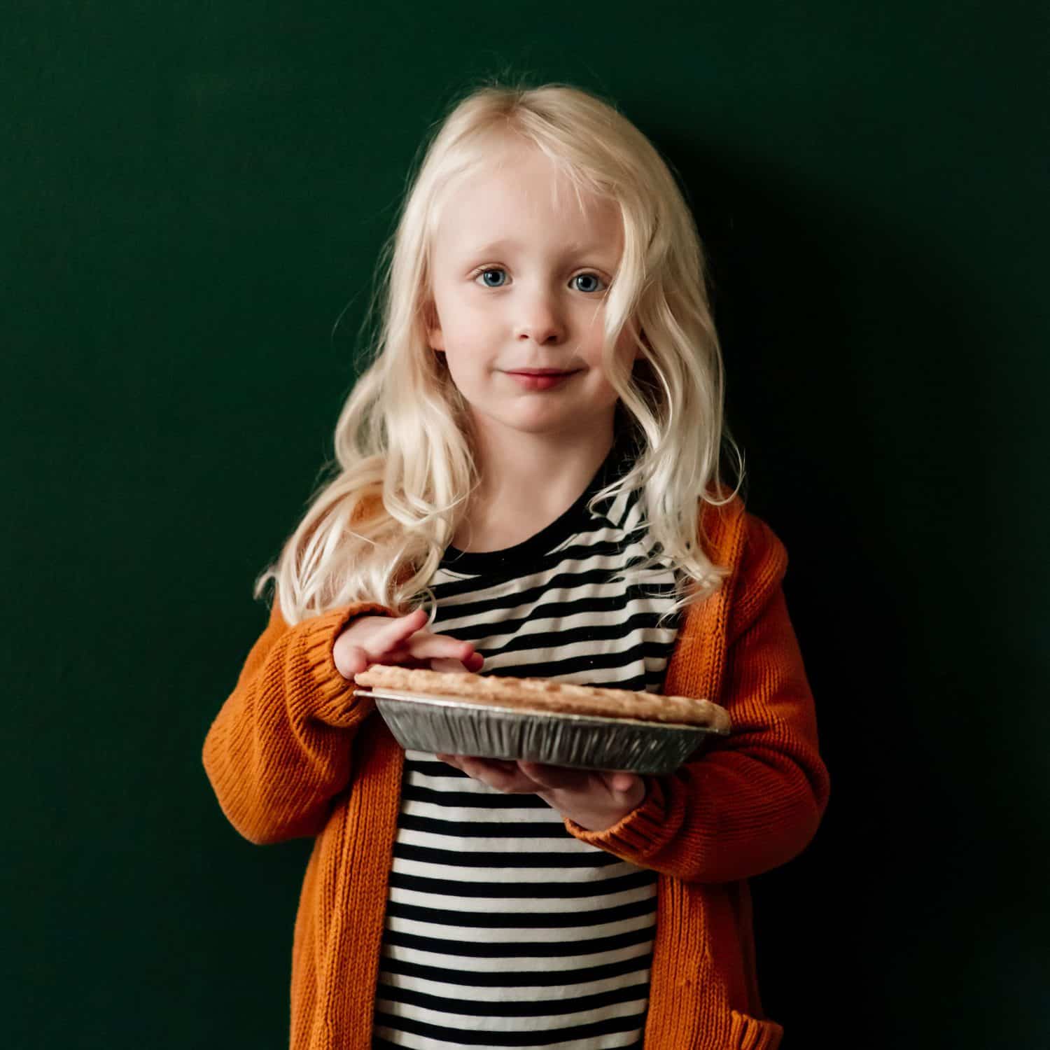 Little girl in an orange sweater smiling while holding a pie