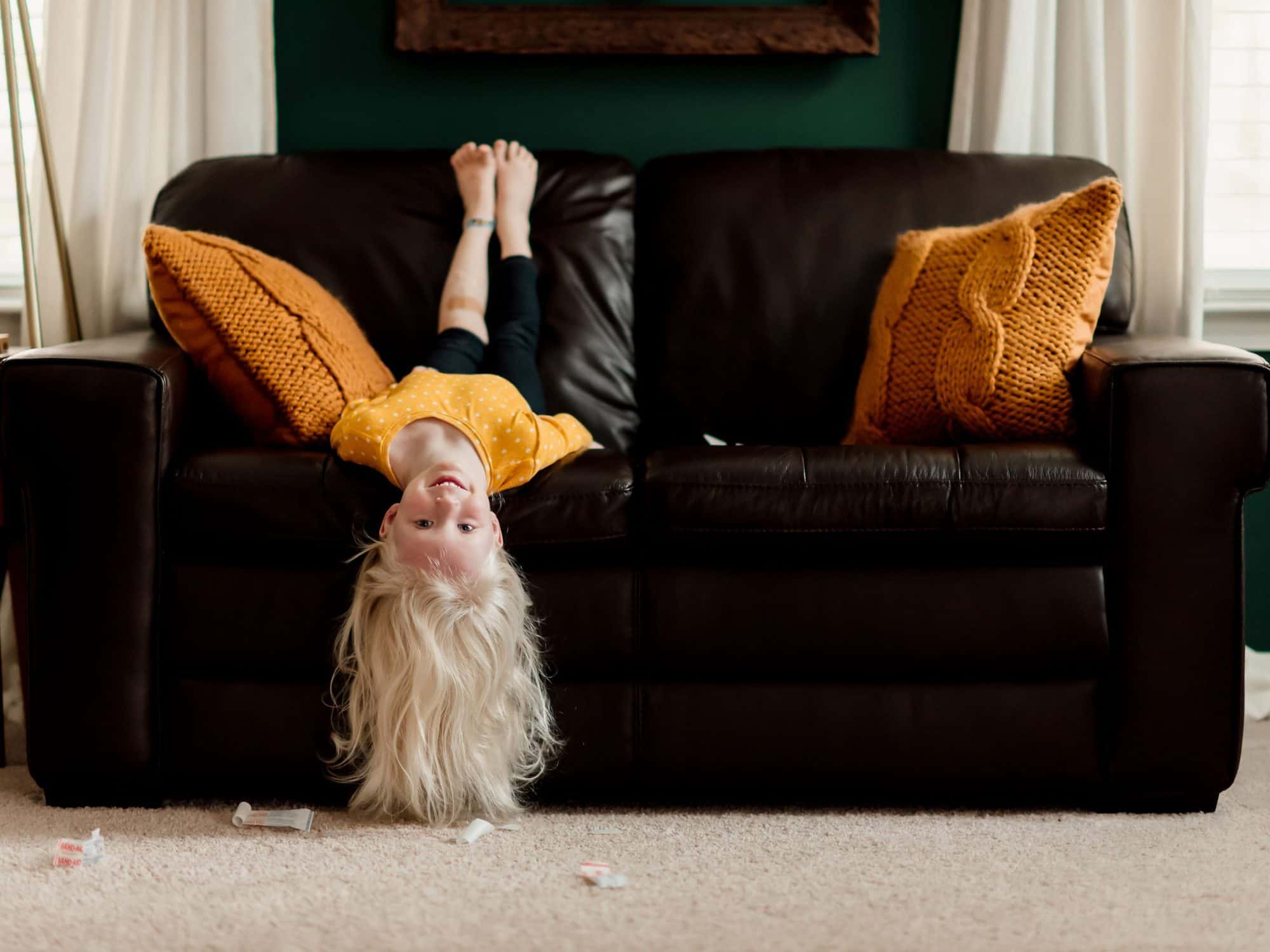 A child hanging off a leather couch upside down 