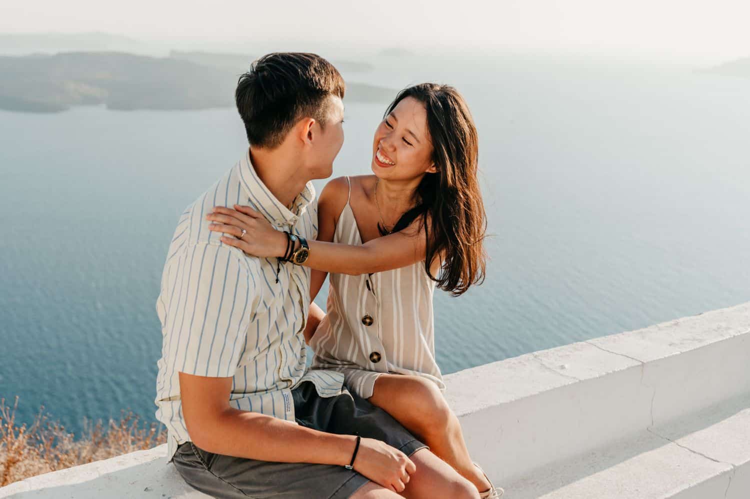 A couple sits on a ledge overlooking the sea