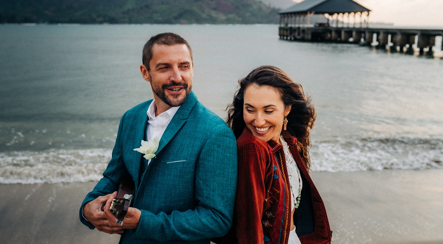 A couple leans in back-to-back while laughing on the beach