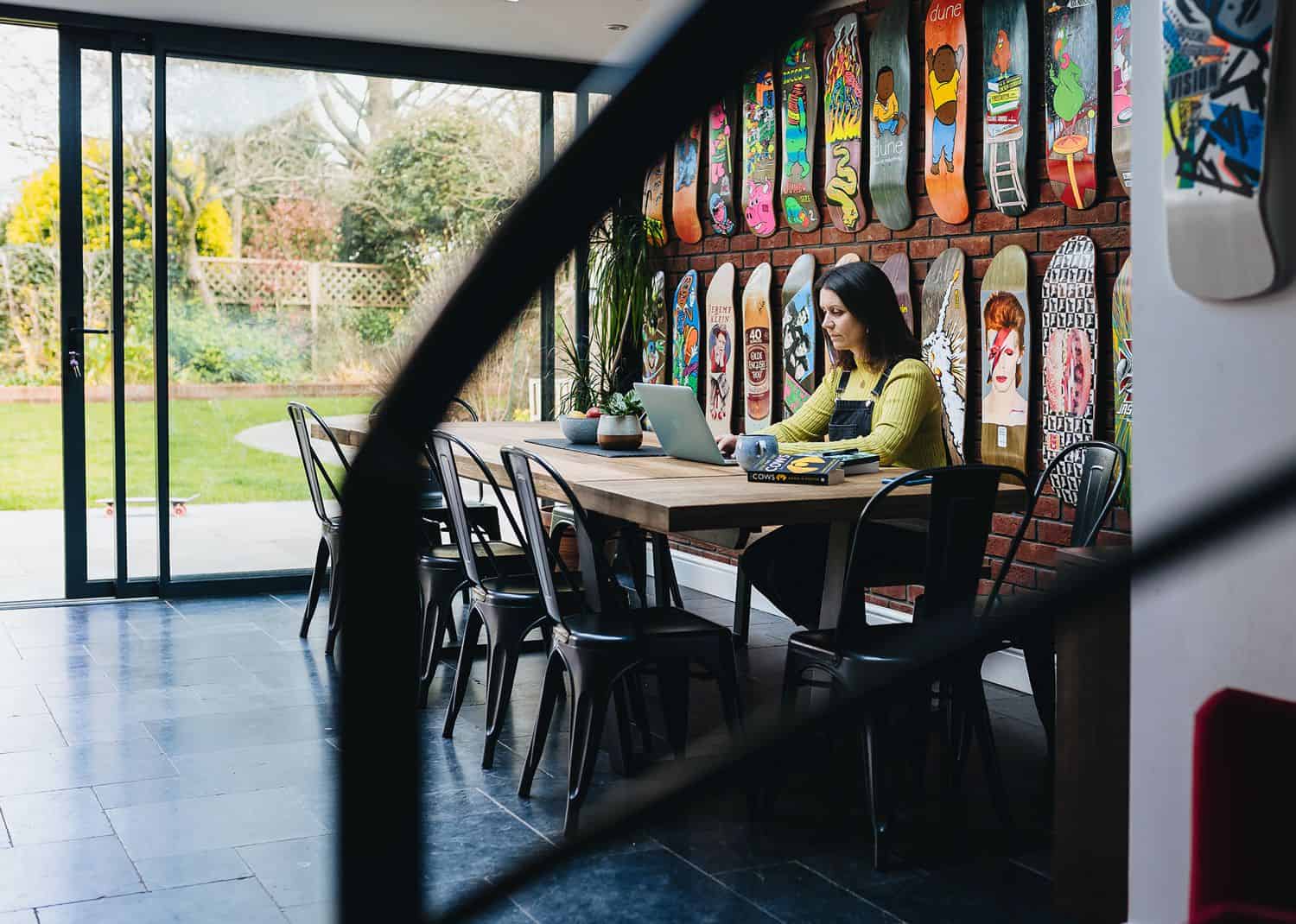 A brunette woman in a lime green shirt sits at a table in front of a wall of skateboard decks