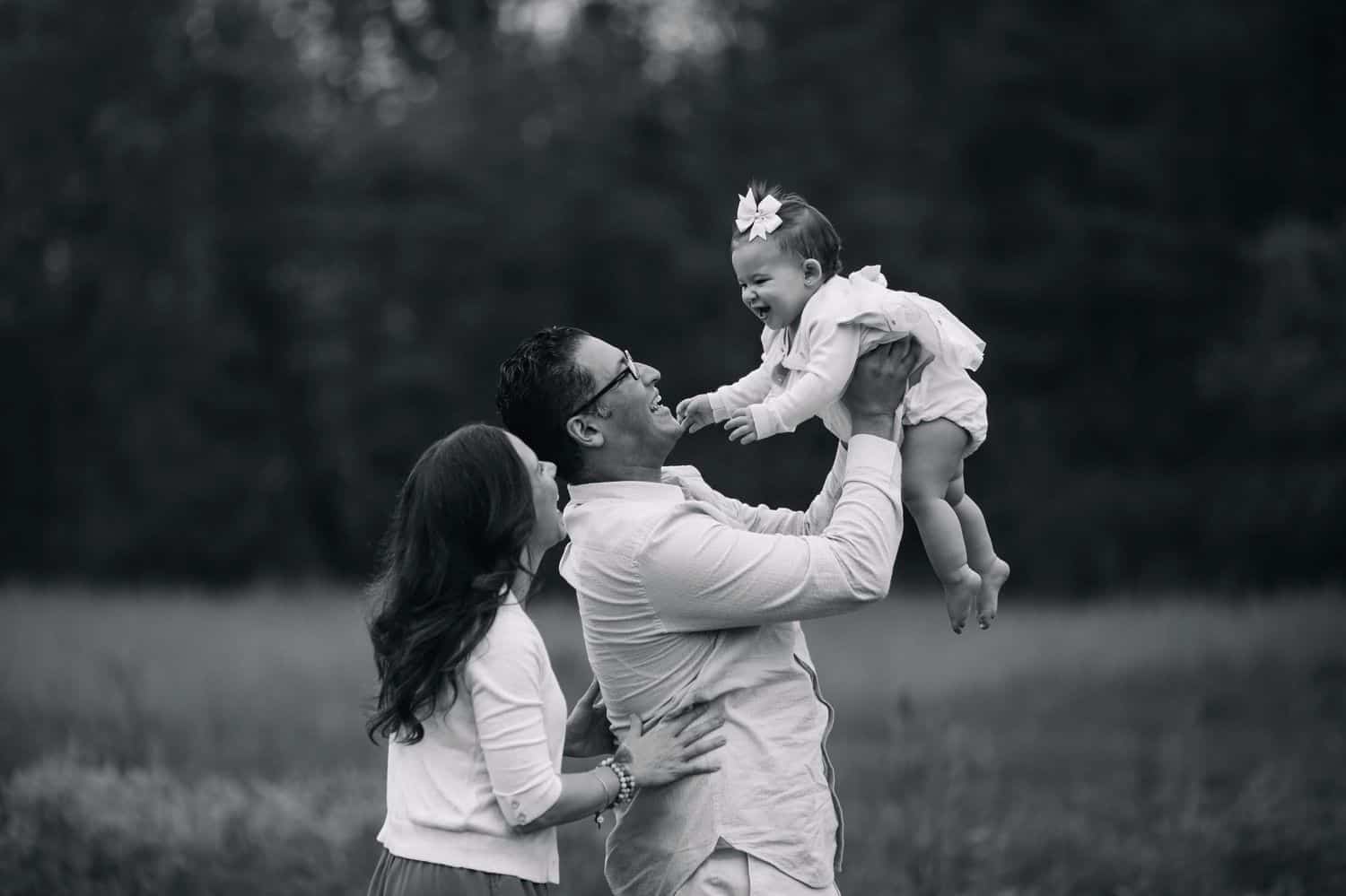 Black and white portrait of two parents lifting their baby daughter into the air