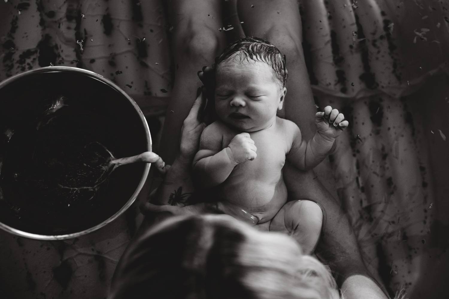 A newborn baby lies on a blanket beside a medical bowl containing the baby's placenta, still attached to the infant by their umbilical cord