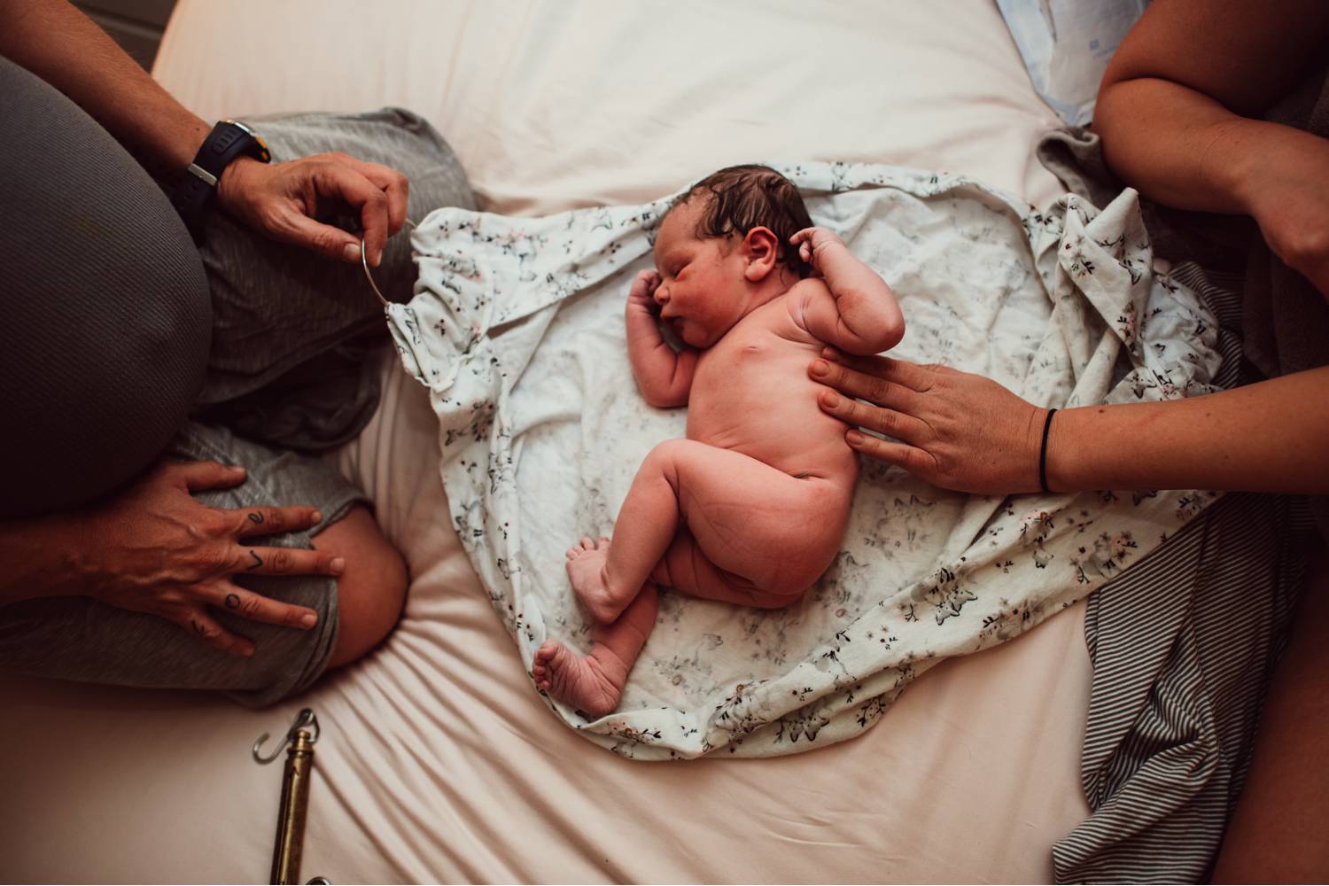 A newborn baby curls up on a blanket as the parents sit on either side of the infant