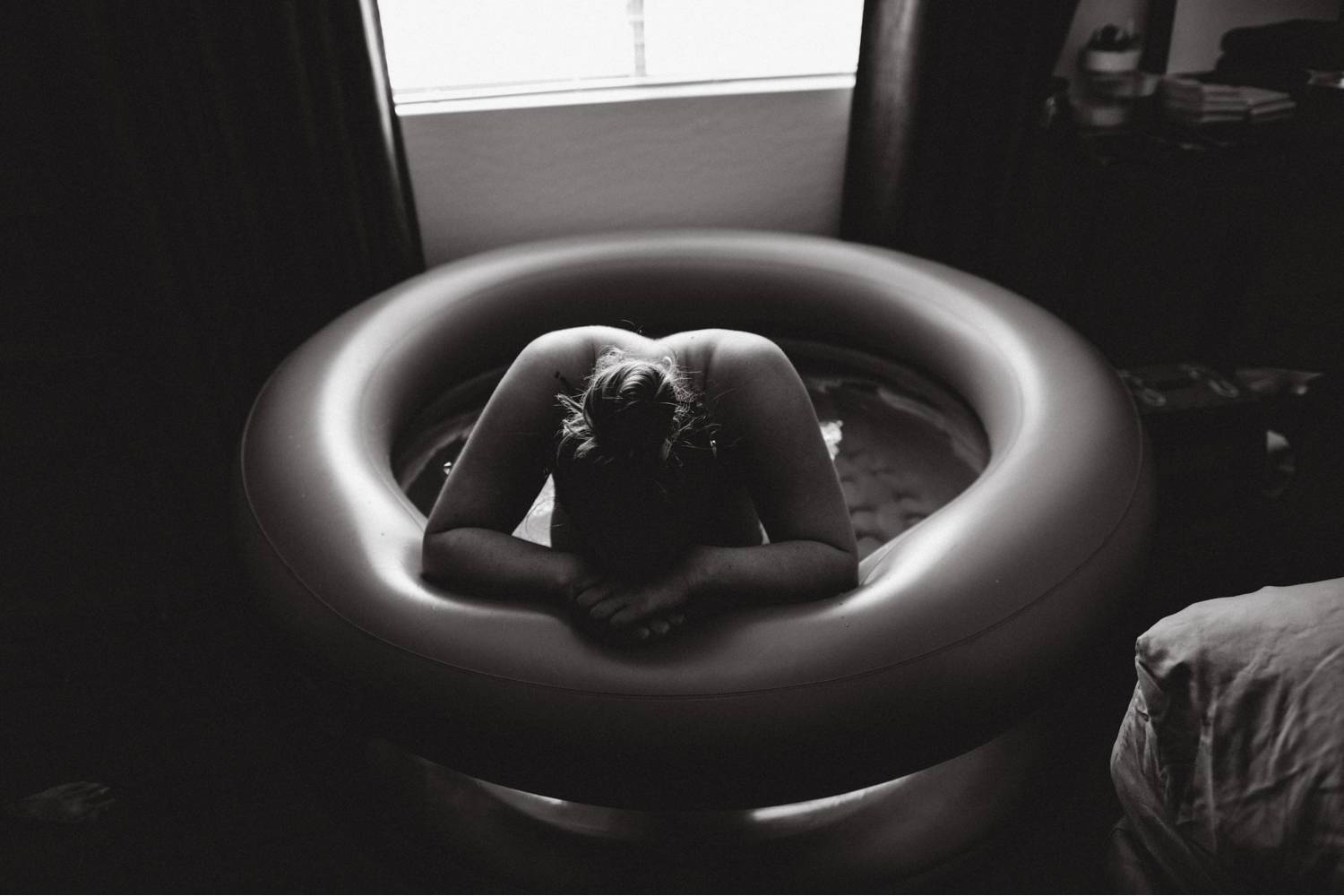 A laboring mother leans on the edge of an inflatable tub during her home birth