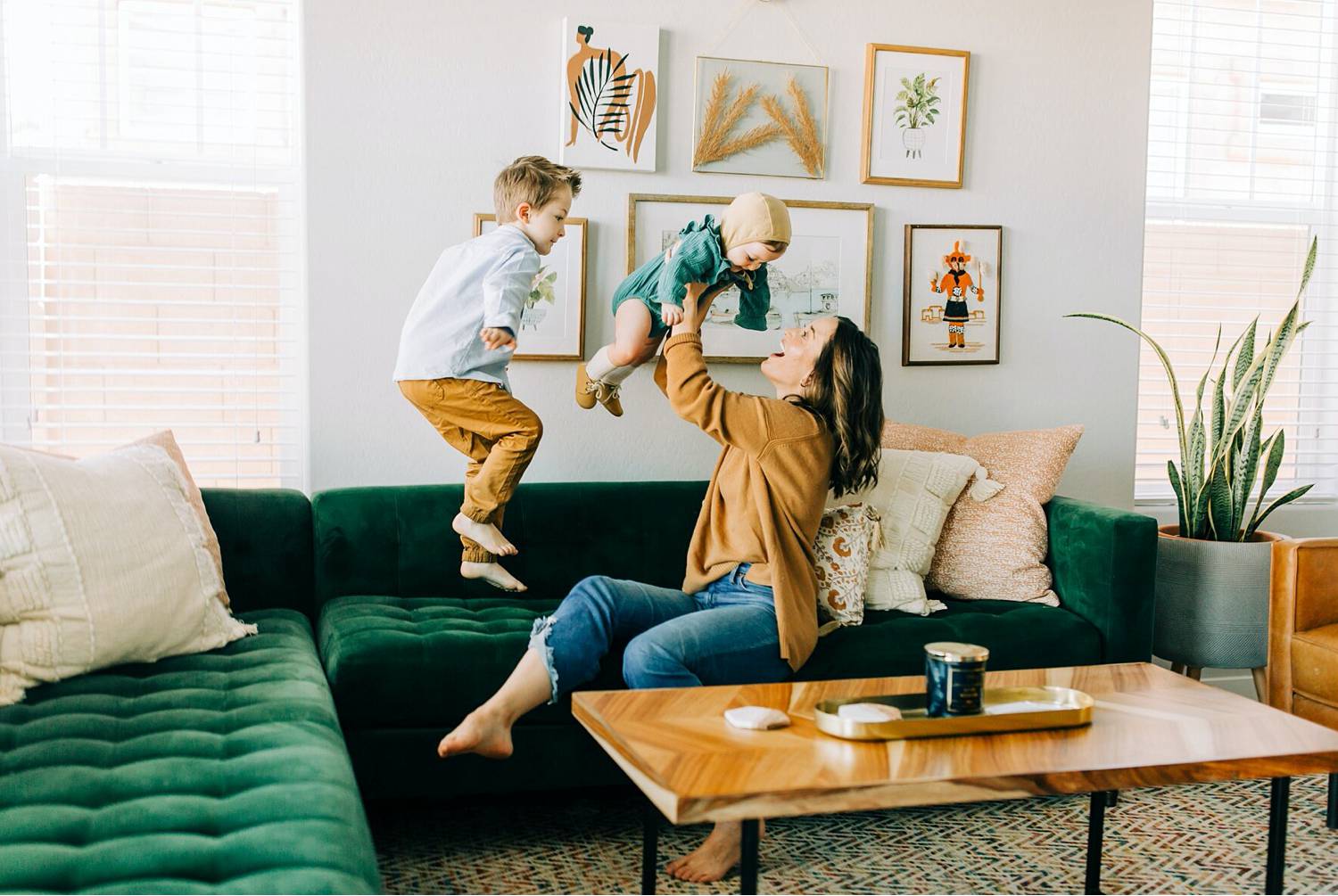 Photo: BreAnne Weston's lifestyle image shows a mom in a yellow shirt lifting her toddler daughter into the air as her young sun jumps on the green velvet sofa next to her.