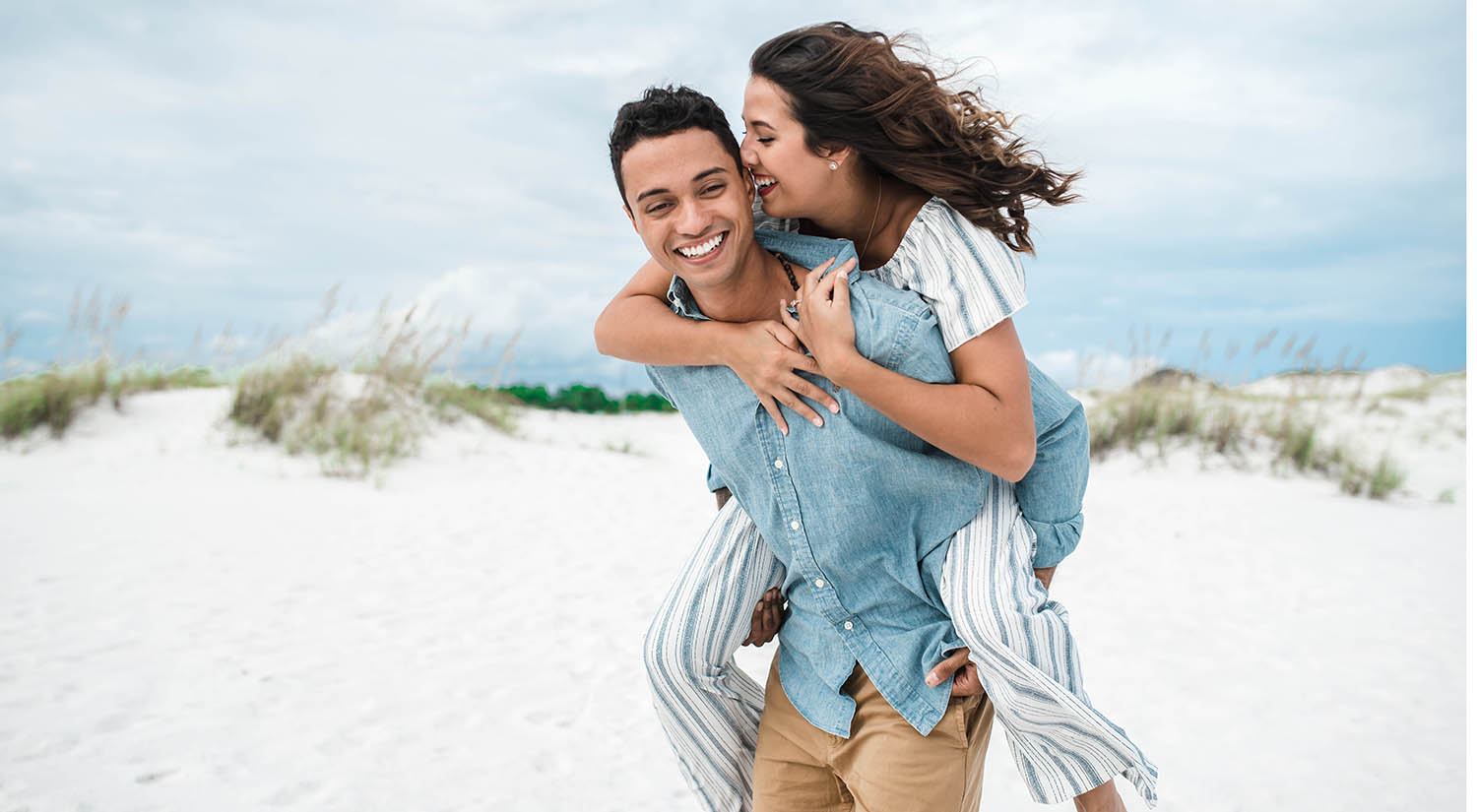 A woman laughs will her husband gives her a piggy-back ride at the beach