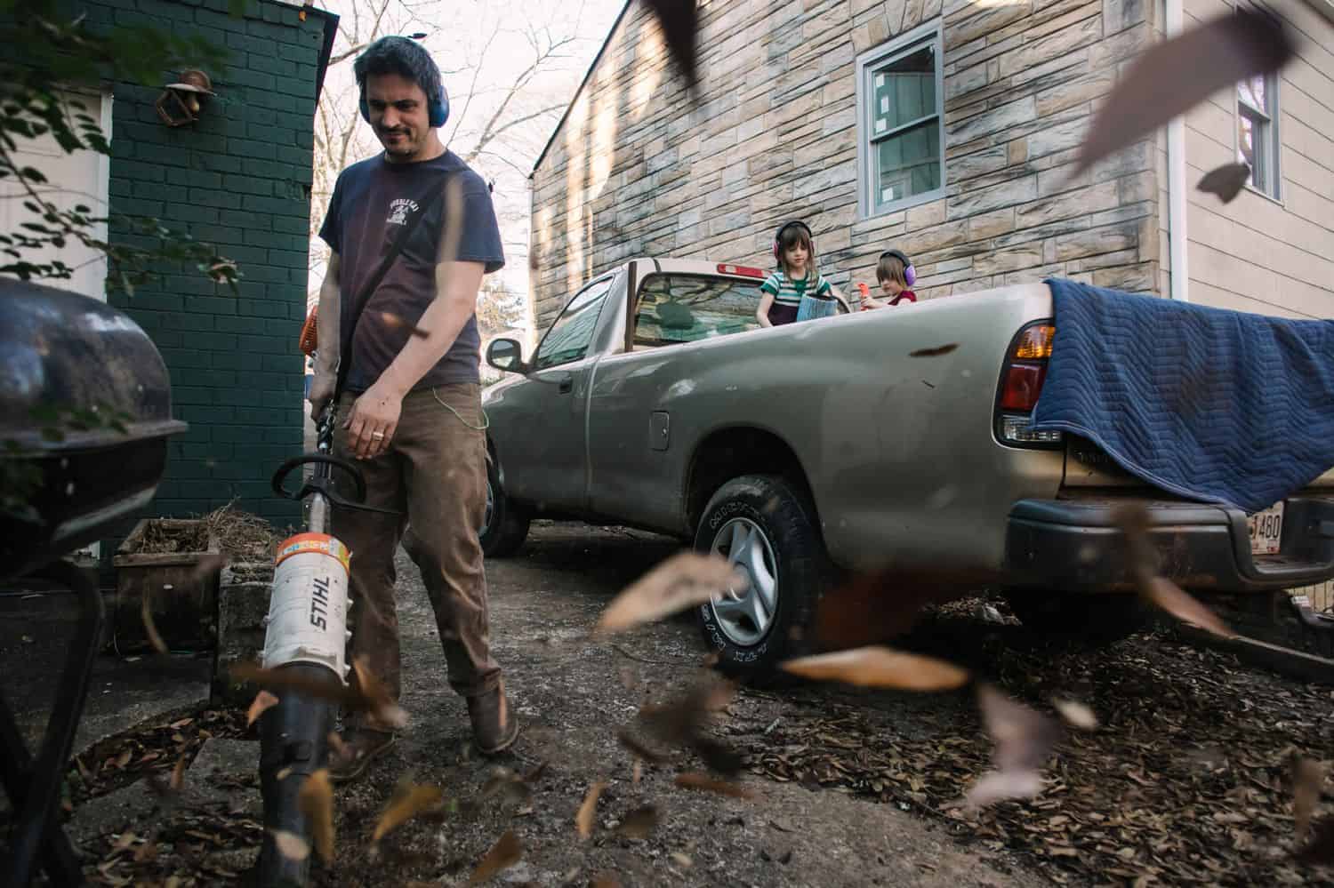 Fearless Family Photos All Have These 4 Ingredients: Lifestyle Photography - Dad Leafblowing the Yard While Daughters Play In the Pickup Truck