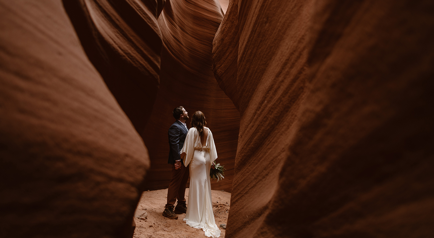 A bride and groom stand in a red rock canyon