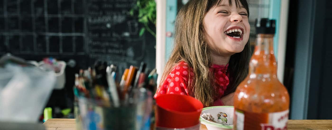 a little girl in a red shirt sits at a kitchen counter laughing