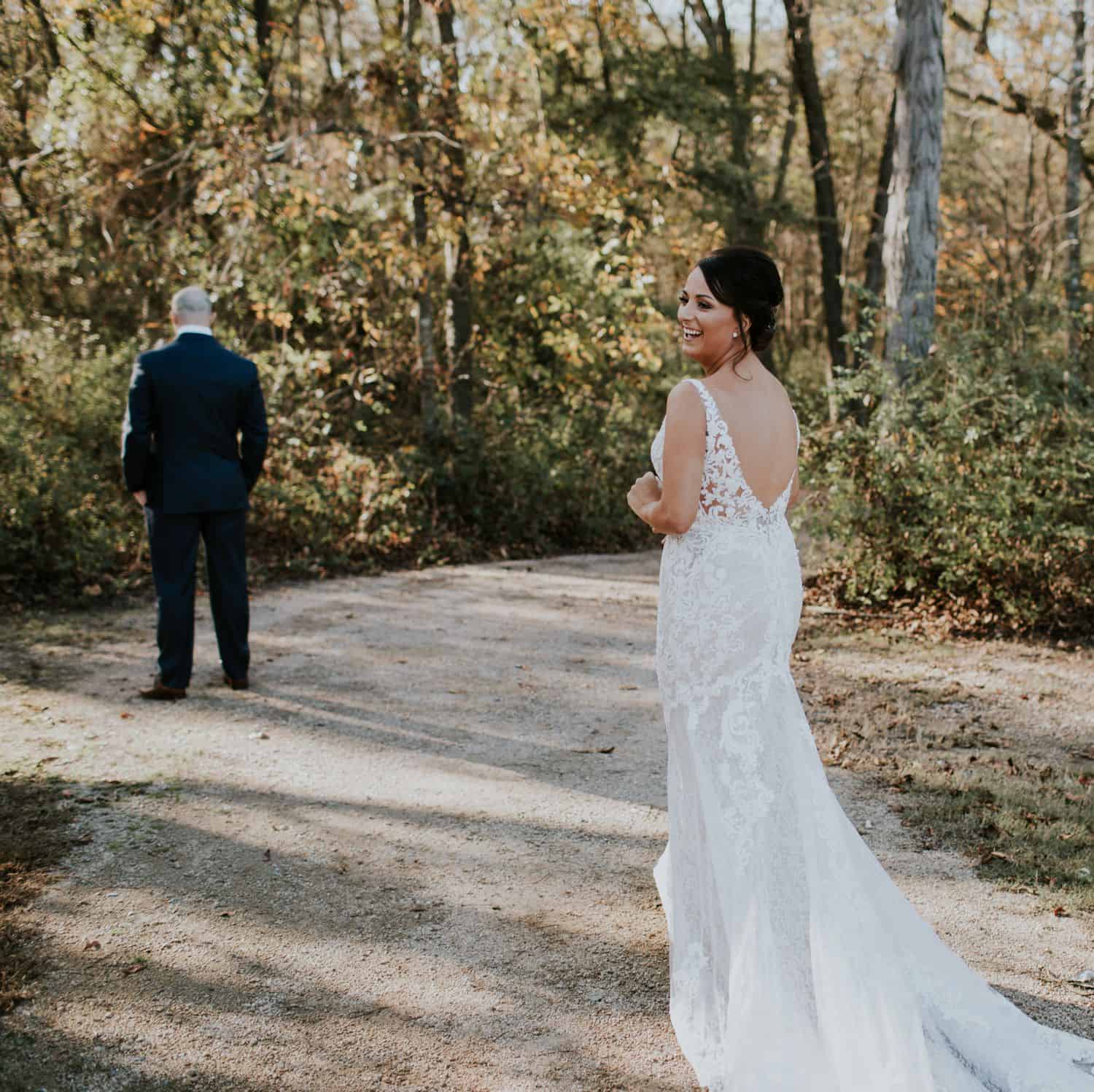 A bride smiles back at the camera as she approaches her groom for their first look.