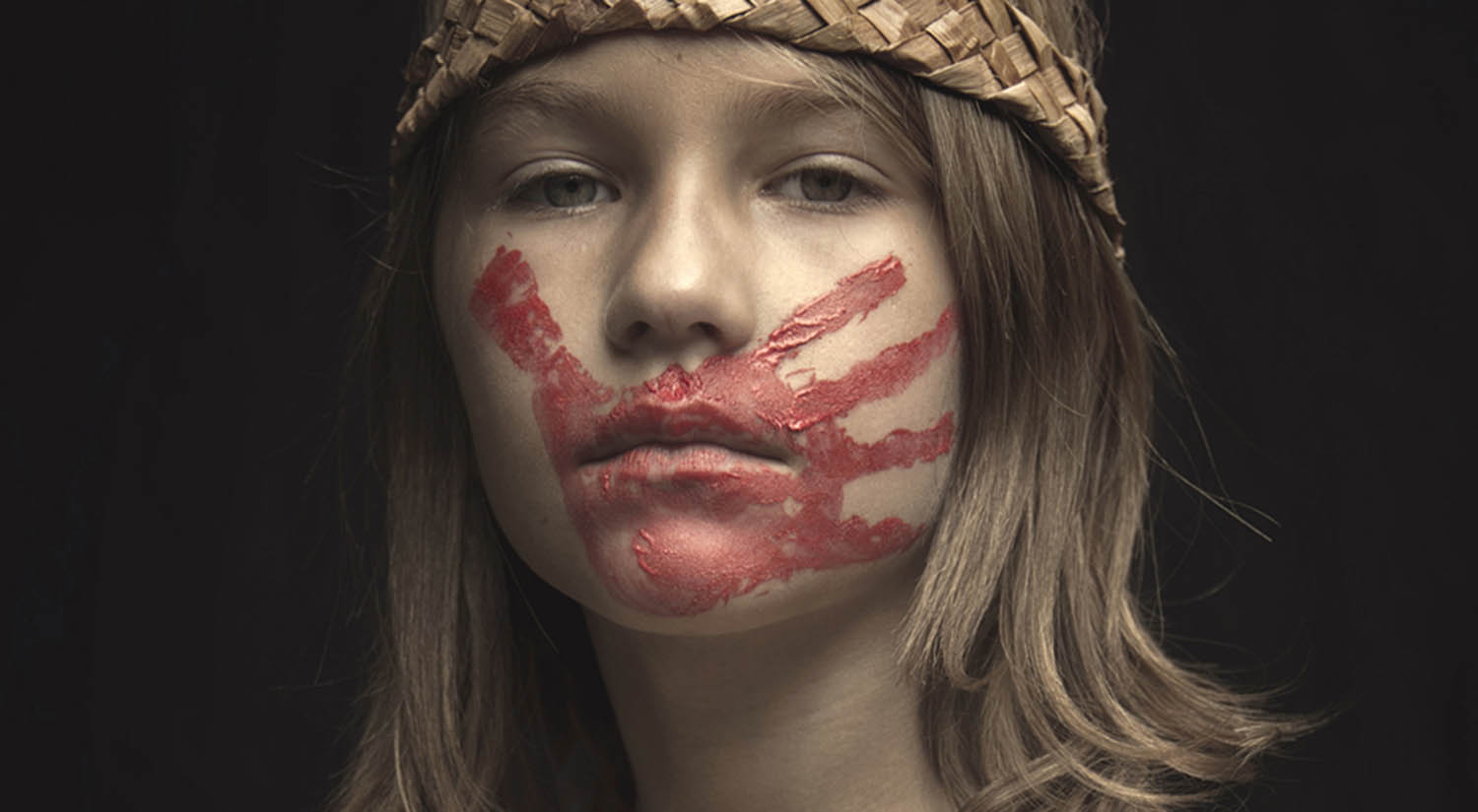 A young girl wears a red handprint across her mouth in honor of America's Missing and Murdered Indigenous Women