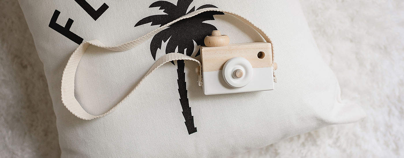 A wooden toy camera rests atop a small pillow bearing a palm tree