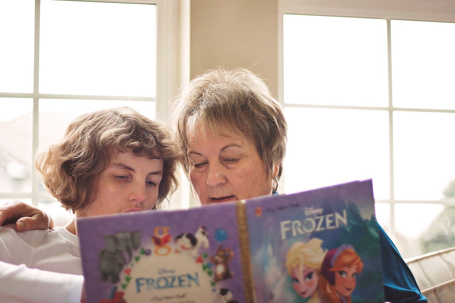 A mom sits on the sofa at home with her special needs daughter reading a book.