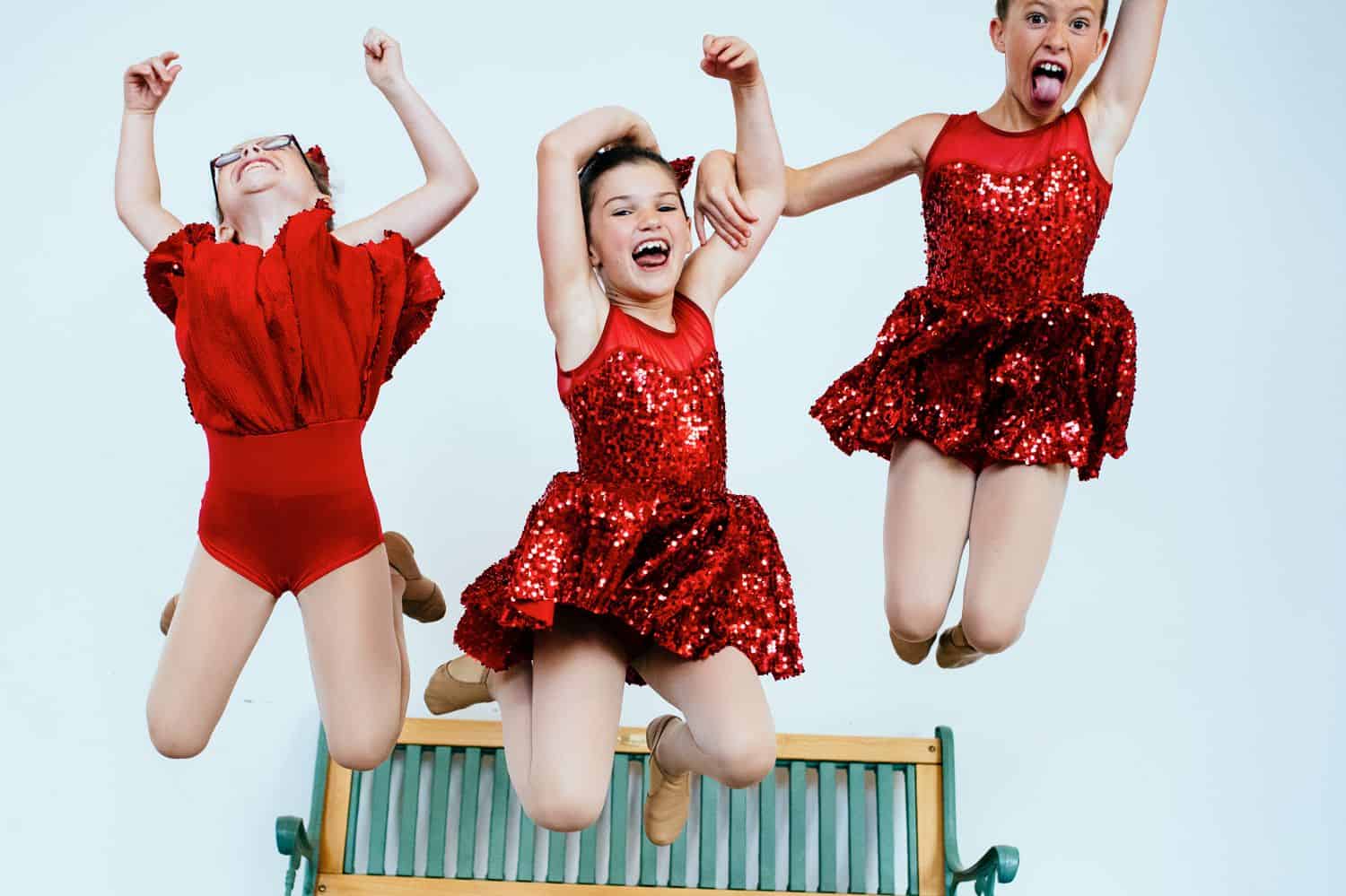 Three little girls in red satin dresses leap into the air with their arms raised toward the sky. By Kate T. Parker for Strong is the New Pretty