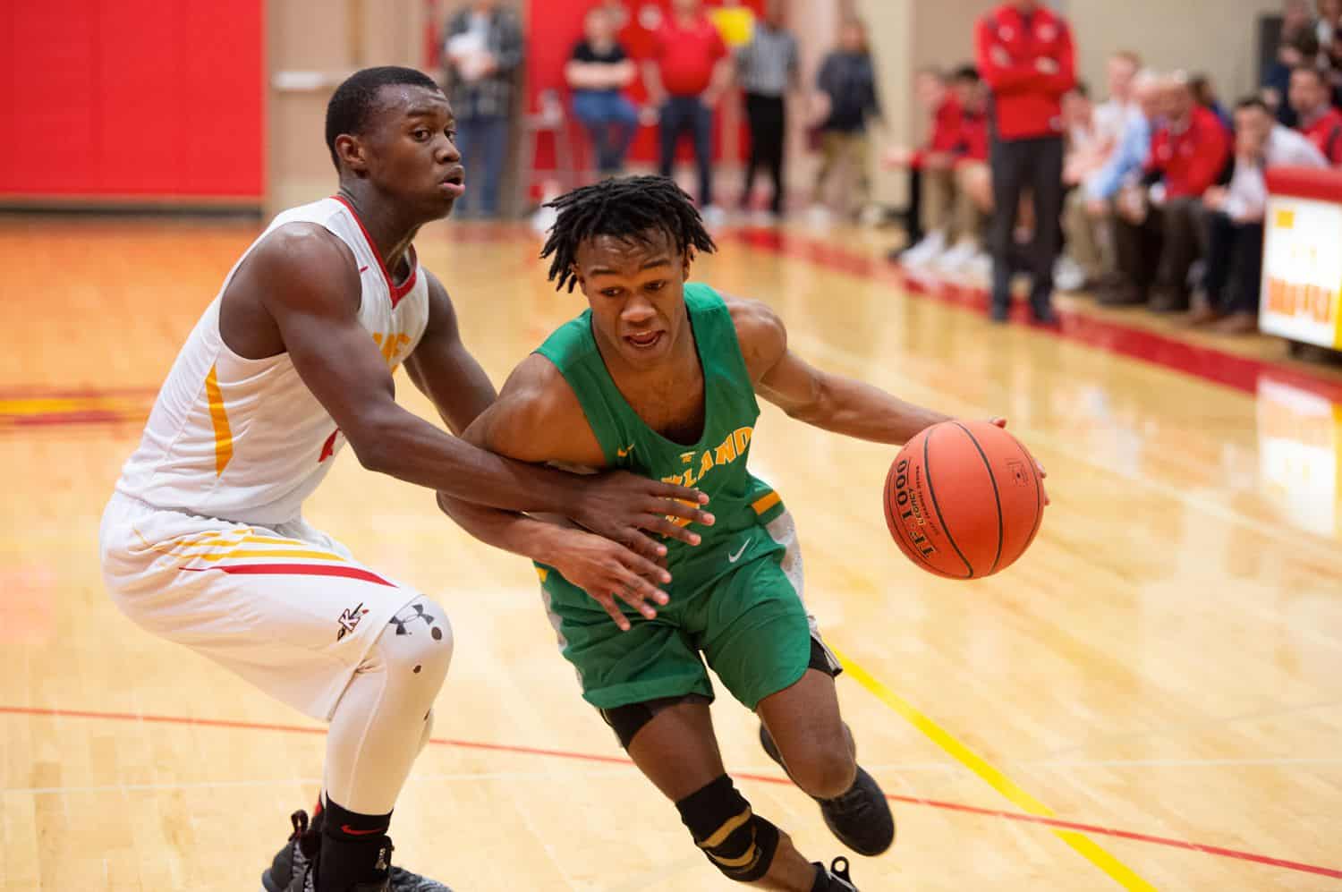 A young man dribbles the basketball across the court and past an opponent 