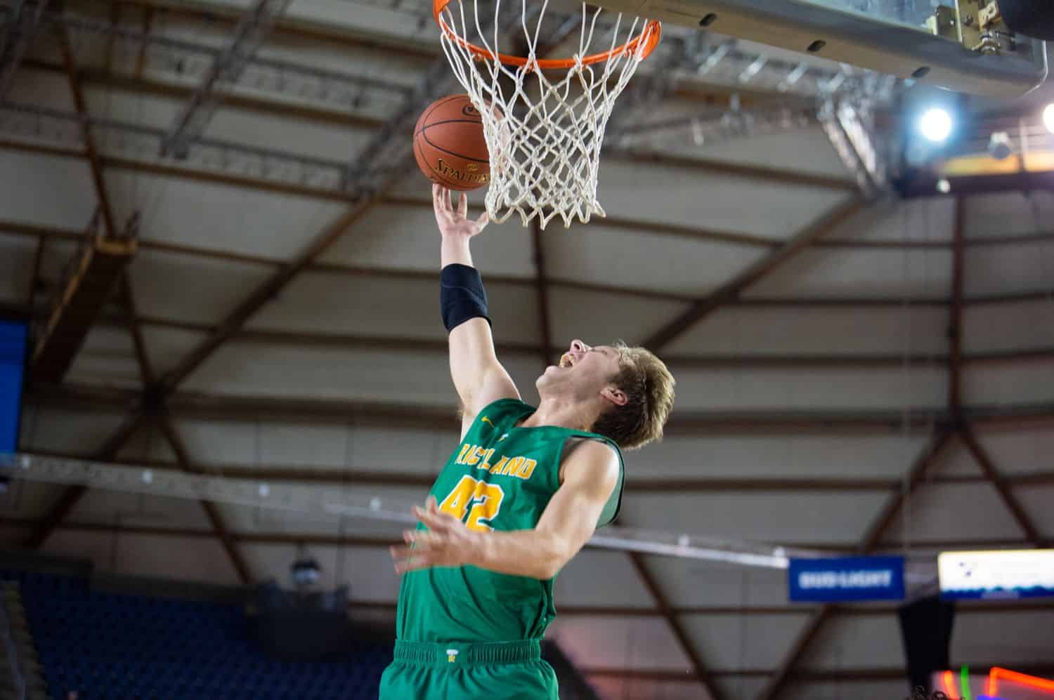 a young man in a green jersey slam-dunks a basketball