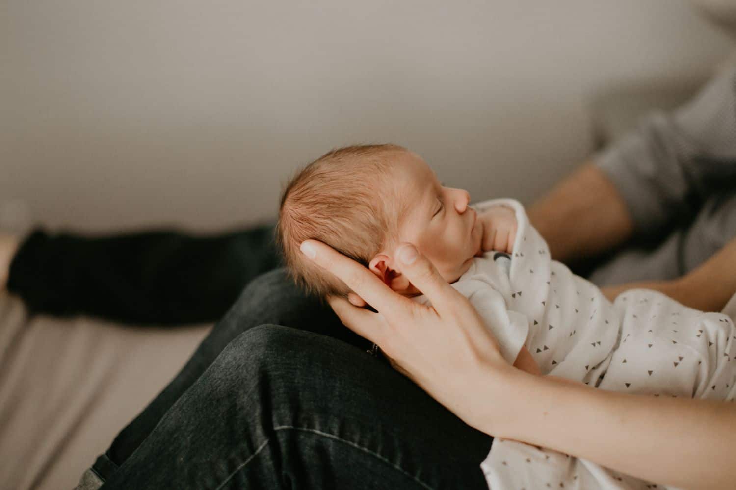 Lifestyle Newborn Photos: A profile photograph of a newborn baby, swaddled and in their mom's arms.