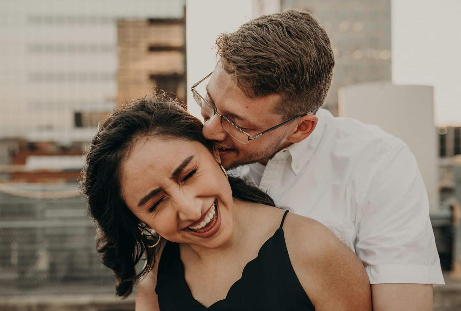 A man nibbles on his girlfriend's ear as she laughs