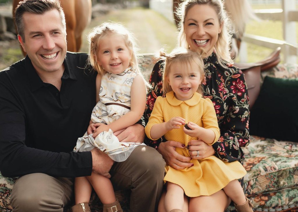 Mariah Gale Creative shoots family of 4 photo poses like this one, where the family sits close together on a vintage sofa and smile at the camera.