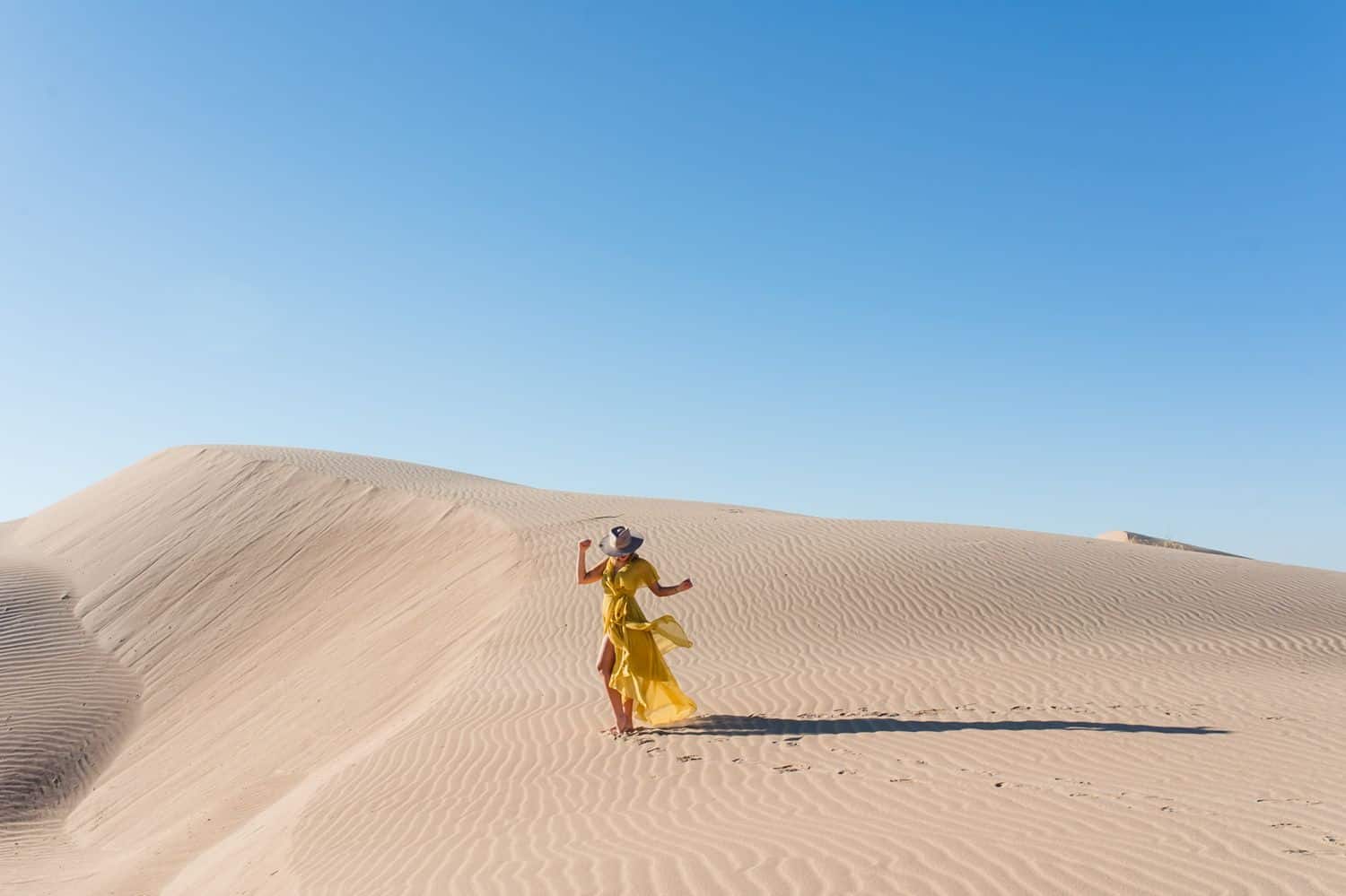 Woman in a yellow dress dancing in the desert.