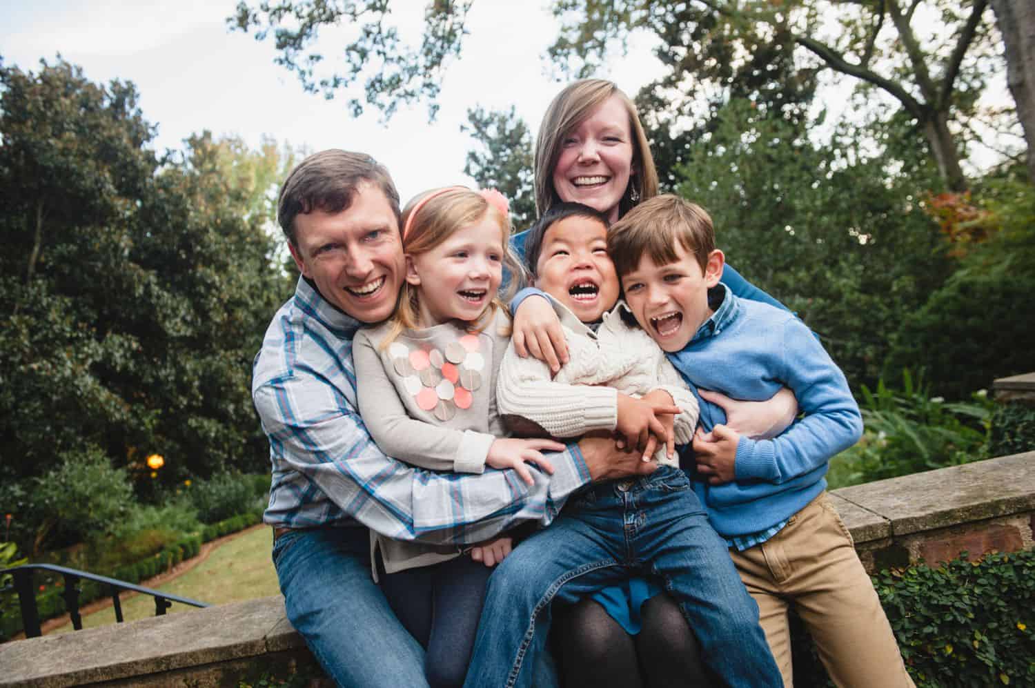 Two parents snuggle and tickle their three children in a park.