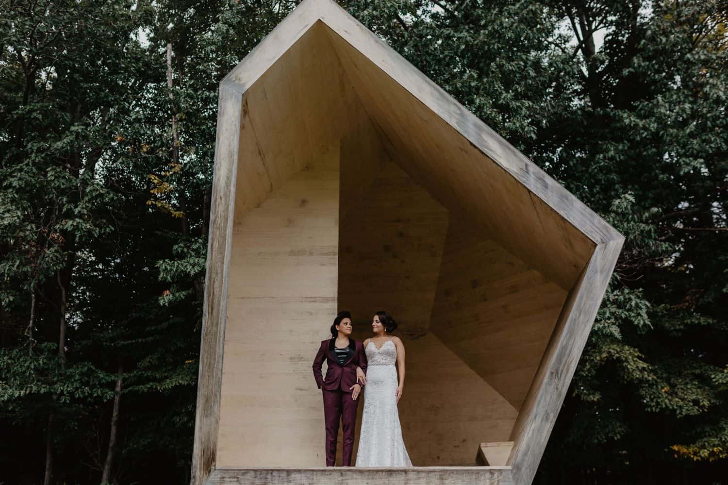 Two women stand in a geometric structure on their wedding day for portraits