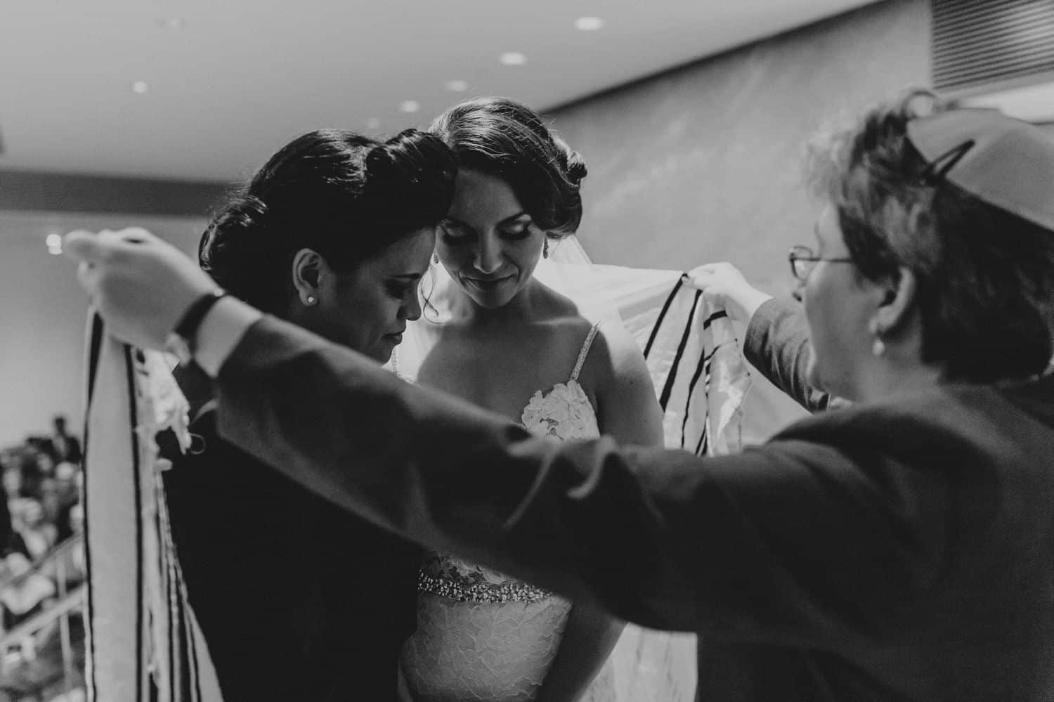 A rabbi holds a prayer shawl around two women during their wedding ceremony