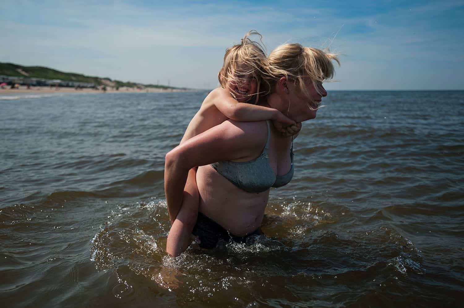 A mom carries her young child on her back through waist-deep lake water