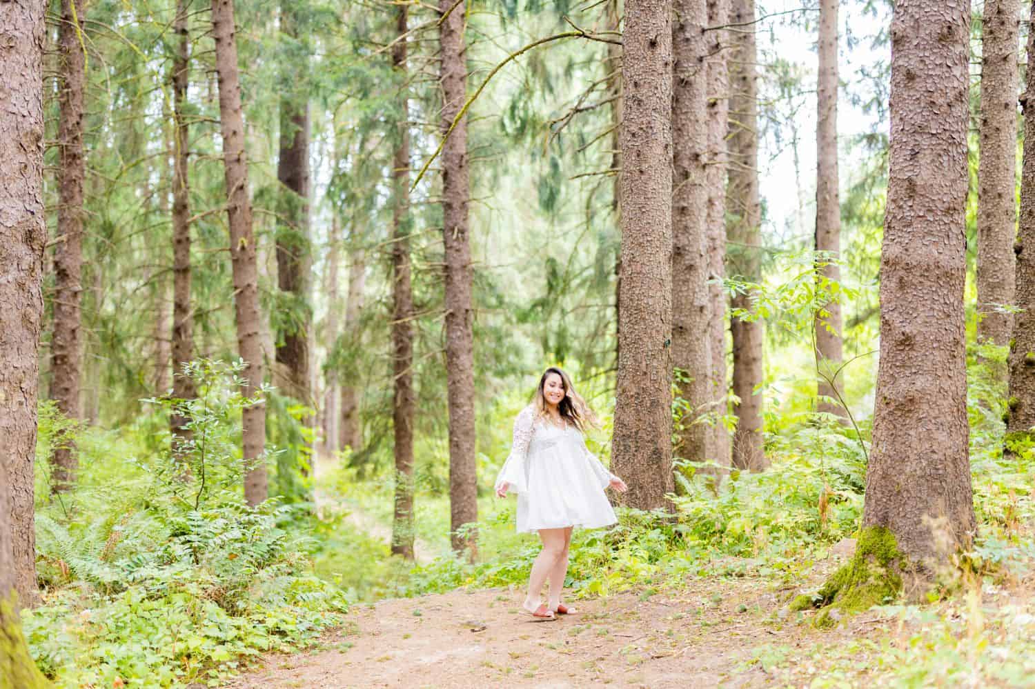 A person in a flowing white dress twirls in the Oregon forest while Sofia Angelina makes photographs