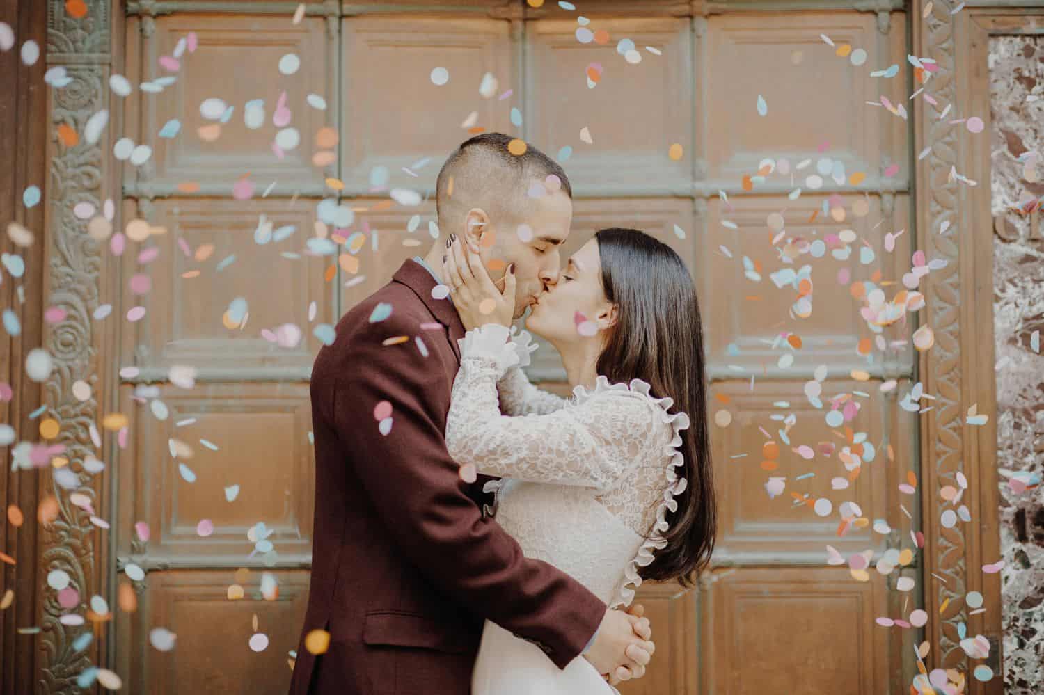 Festively dressed newlyweds kiss amid a storm of confetti.