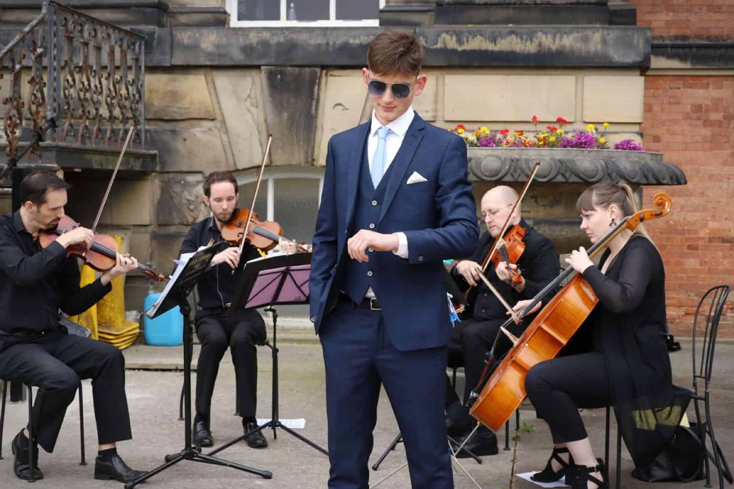 A high school senior boy poses with a string quartet for his prom photography