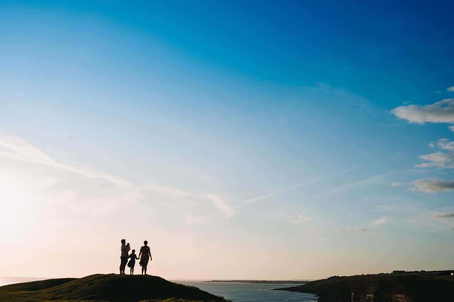 Silhouette of a family standing on a hill overlooking the ocean.
