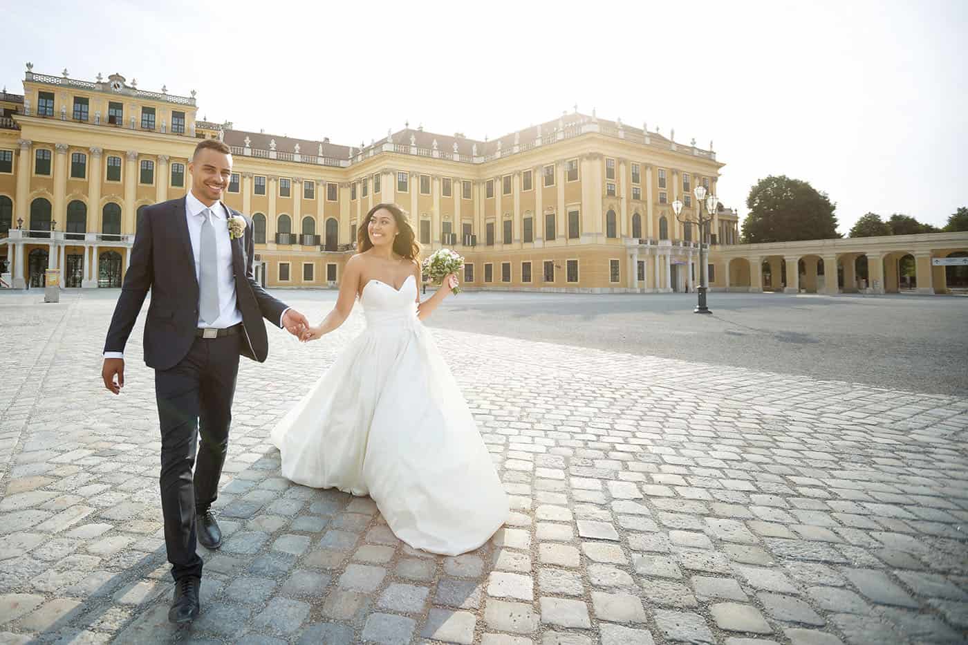 This is the Key to Amazing Client Relationships | A bride and groom stroll through a massive stone courtyard as the sun pours over them.