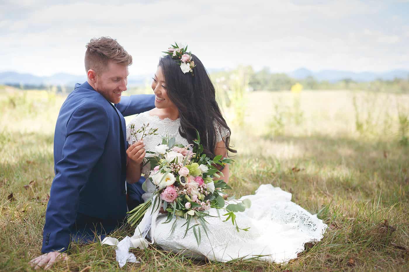 A bride and groom sit together in a field full of wildflowers.