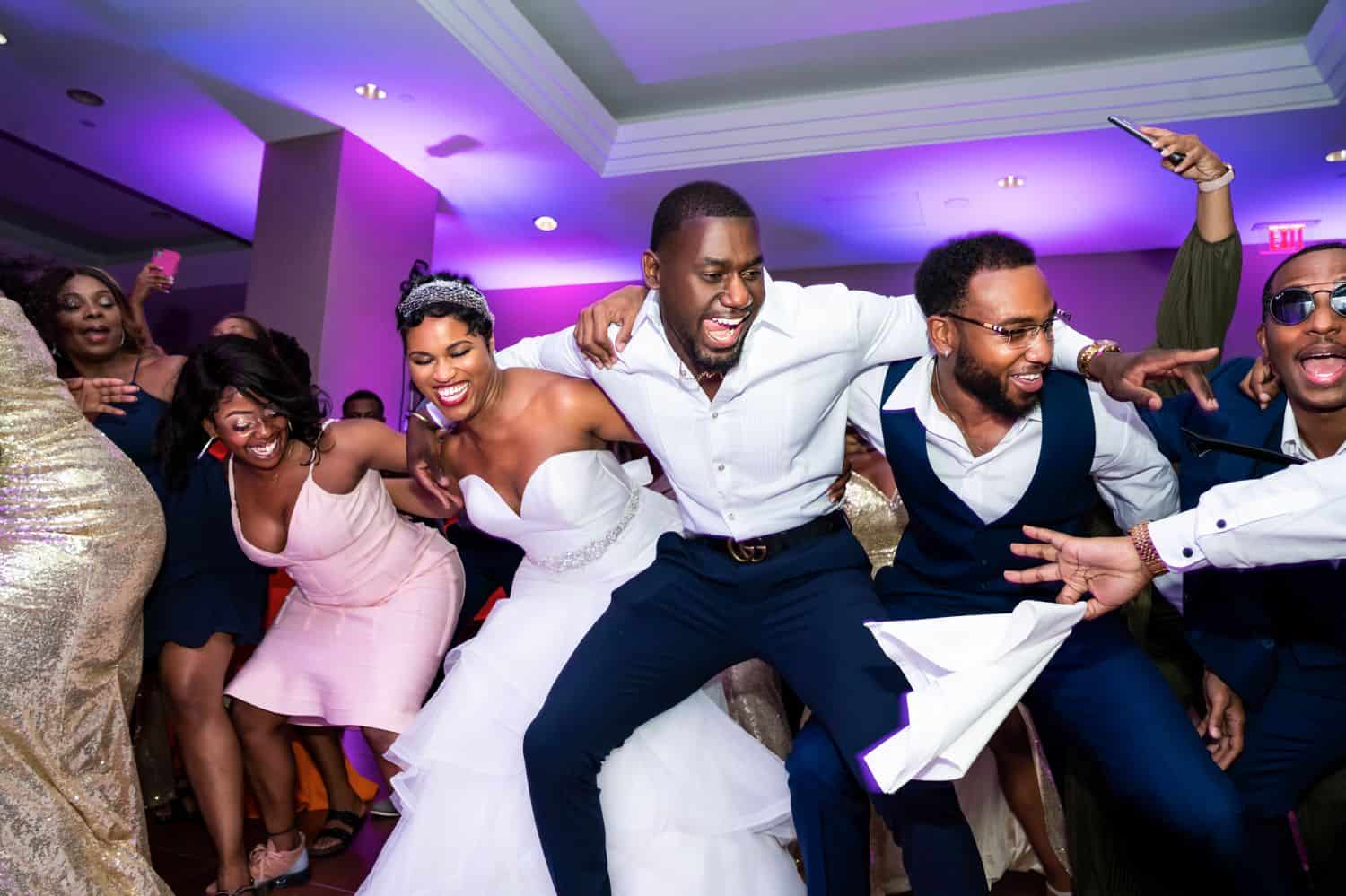 A bride and groom dance happily in a circle with their friends.