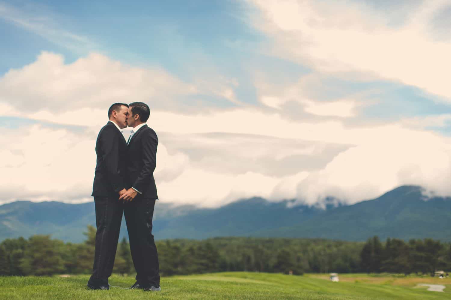 Two grooms kissing in an open field. By Harris & Co.