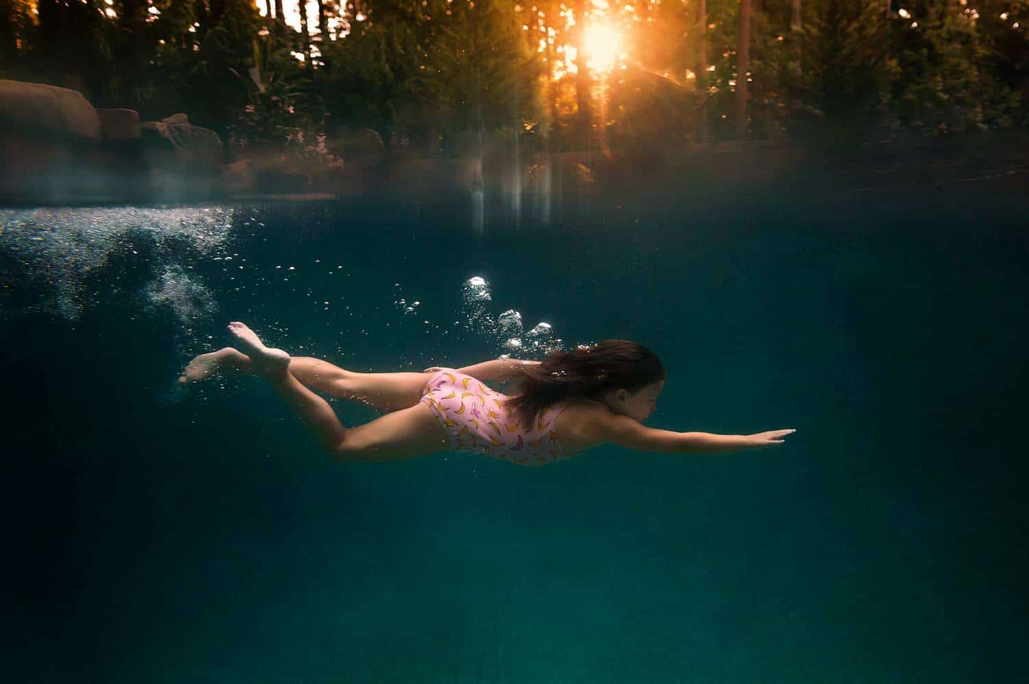 A child in a pink swimsuit swims underwater with one arm outstretched