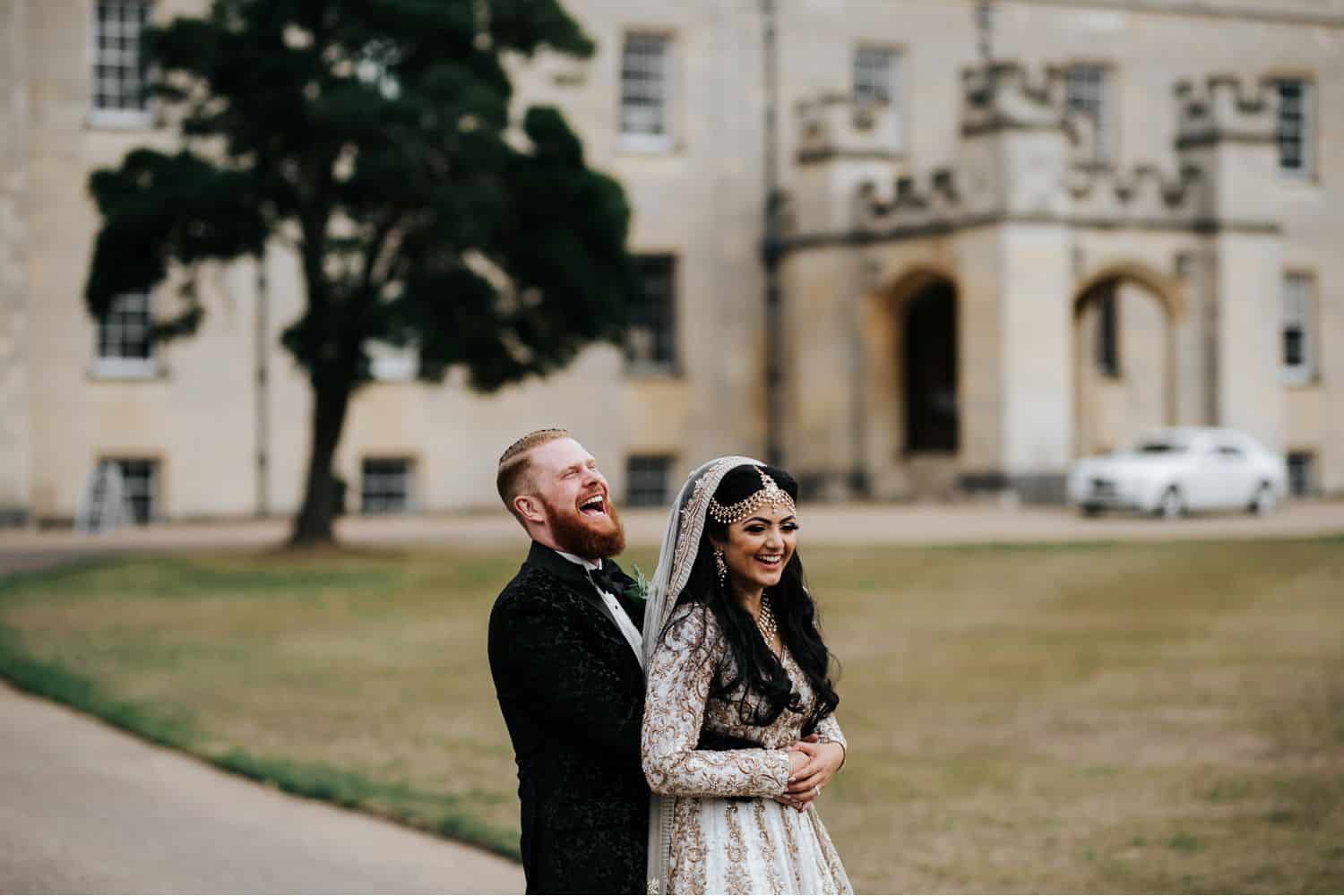 Wedding Print Packages: Bearded groom stands behind bride dressed in traditional Indian wedding attire. A castle is in the background.