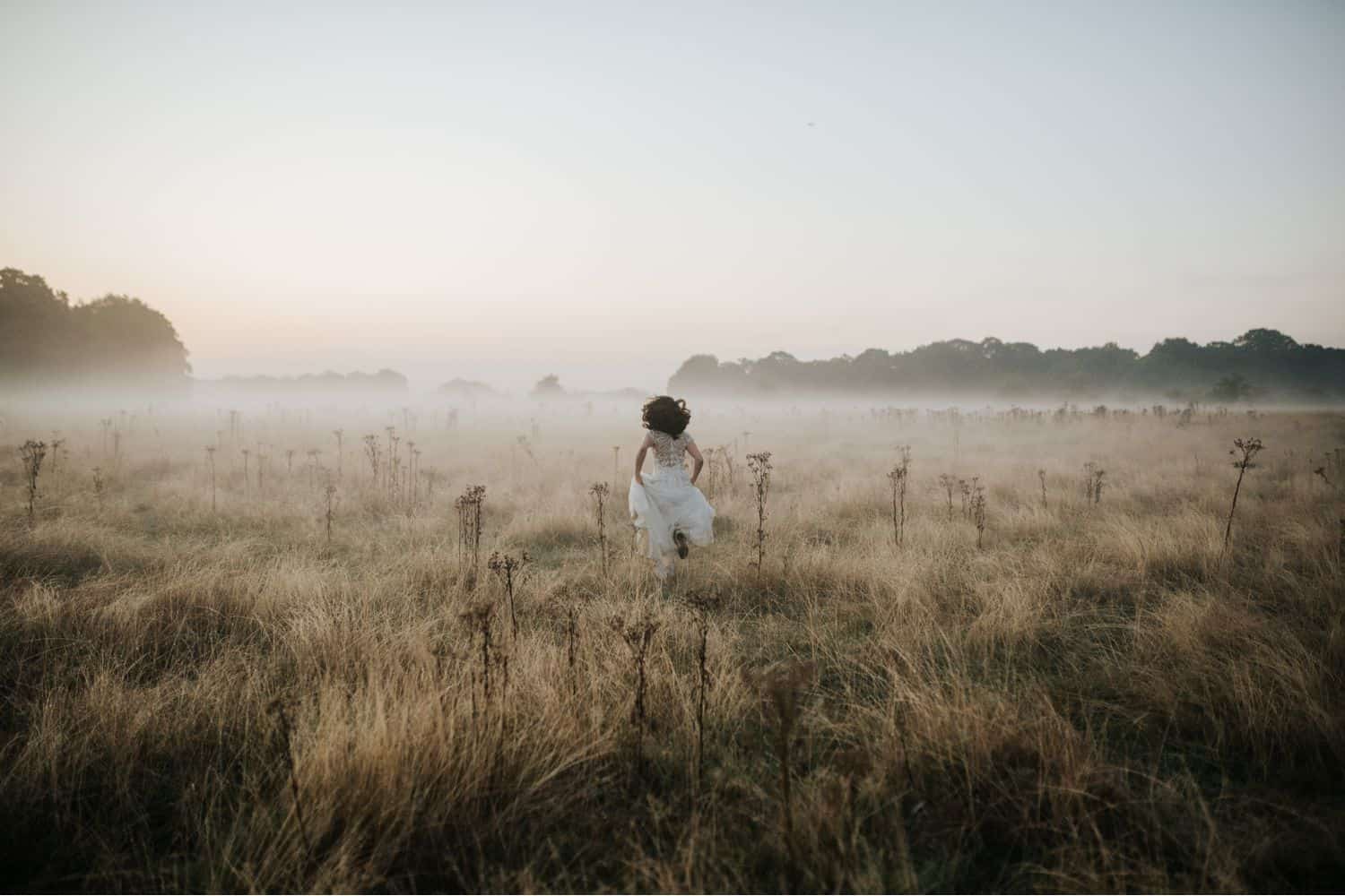 Wedding Print Packages: A bride runs away from the camera through a misty field.