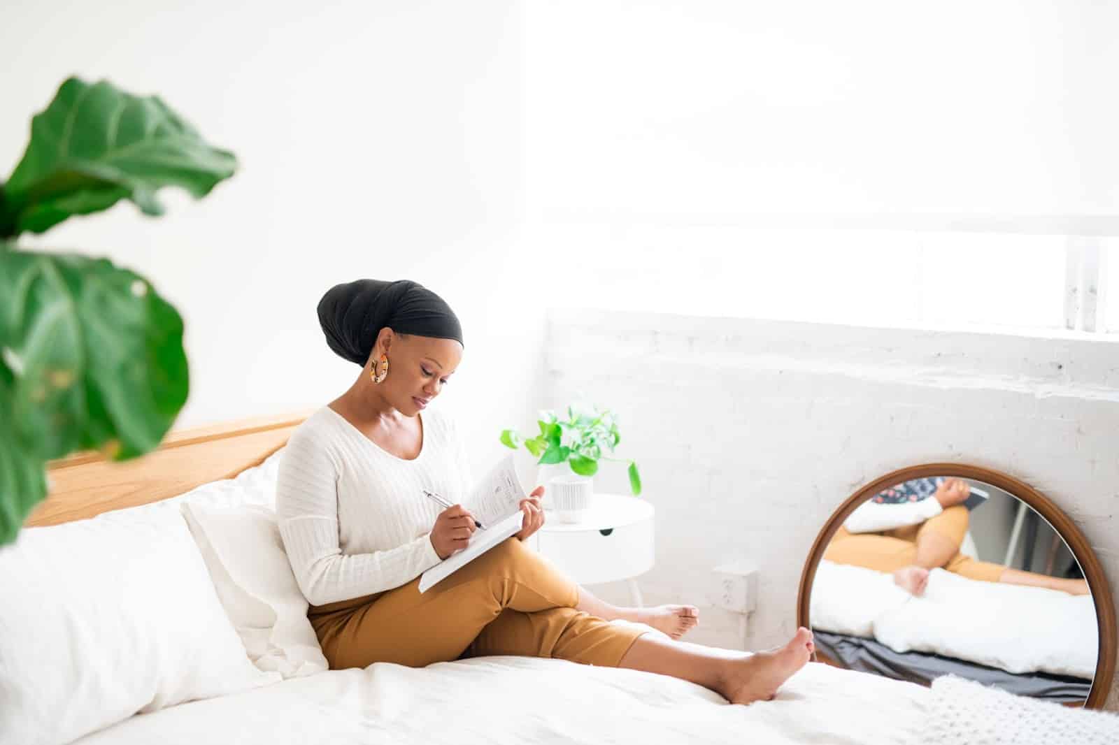 Lifestyle photo of woman sitting on a bed writing in a journal